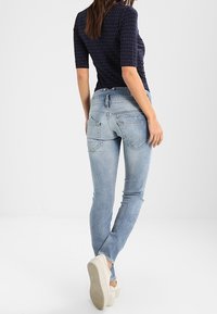 Jeans blu slim-fit in denim, con tasche posteriori, lavaggio sbiadito e vita media, abbinati a calzature chiare.