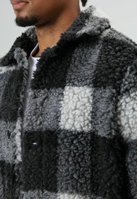 Grijs en zwart geruit fleecejack met een getextureerd, pluizig oppervlak, voorzien van grote knopen en een kraag, voor warmte en comfort.