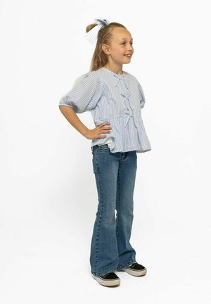 Ljusblå randig kortärmad blus med sidoknytning, kombinerad med utsvängda denimjeans och svarta sneakers. Håret stylat med en matchande rosett.