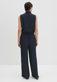 Mouwloze marineblauwe jumpsuit met een hoge kraag, elastische tailleband en wijde broekspijpen. Soepele stof met een relaxte pasvorm.