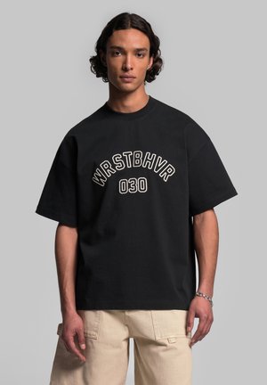 Černé oversized tričko s bílým vyšitým textem "WRSTBHV" a "030" na přední straně. Měkká bavlněná tkanina a krátké rukávy.