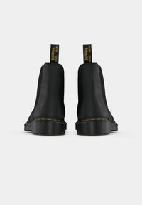 Bottes basses en cuir noir avec une finition texturée, des coutures jaunes et des languettes portant l'inscription "WITH BOUNCING SOLES". Bout arrondi et semelle épaisse.