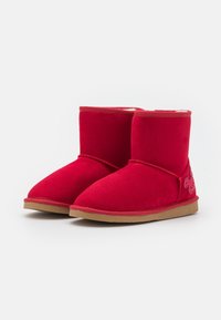 Bottines en suede roux avec une texture lisse, bout arrondi et semelle en caoutchouc. Présente un design décoratif sur le côté extérieur.