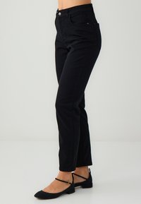 Czarne spodnie dżinsowe z wysokim stanem i dopasowanym krojem, posiadające pięć kieszeni, zapięcie na guzik z przodu oraz miękki materiał dżinsowy. W połączeniu z czarnymi balerinami.