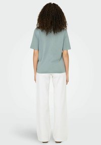 Camiseta de manga corta azul claro, hecha de tela suave, combinada con pantalones anchos blancos, vista desde la espalda.
