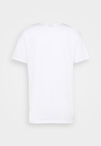 Camiseta blanca de manga corta mostrada por la parte de atrás sobre un fondo neutral claro.