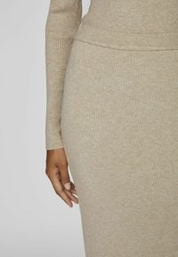 Robe en tricot beige avec une texture côtelée. Le gros plan montre des manches ajustées et une taille avec une finition lisse.