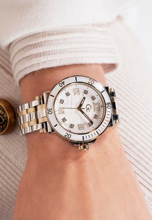 Kerek óra fehér, texturált számlappal, arany és ezüst rozsdamentes acél szíjjal, római számjegy jelölőkkel és korona a szélén.