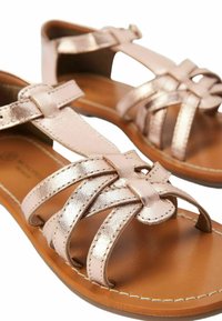Sandales en cuir rose gold avec plusieurs brides entrecroisées, une semelle en cuir marron et un détail de talon compensé bas. Accents cousus visibles.