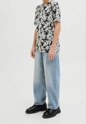 Camiseta negra de manga corta con estampado floral y patrones de hojas blancas, combinada con jeans anchos azul claro y zapatillas negras, posando sobre un fondo neutro.