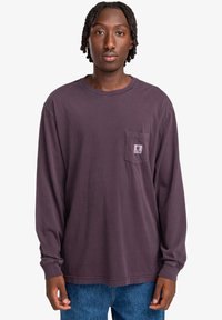 Long-sleeve purple cotton shirt with a chest pocket. Features a crew neckline and a relaxed fit, paired with blue denim jeans.