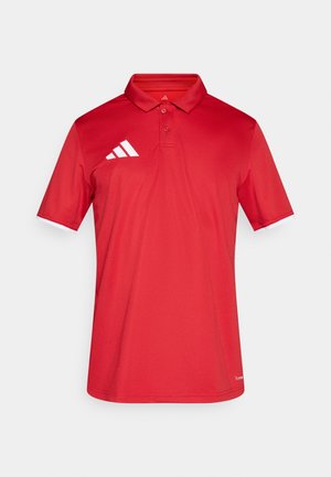 Polo rossa realizzata in tessuto leggero. Presenta un colletto, maniche corte e il logo a tre strisce bianche sul lato sinistro del petto.