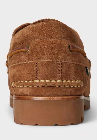 Bruine suède loafers met gestikte details, veters aan de zijkanten en een stevige rubberen zool, gezien van de achterkant.