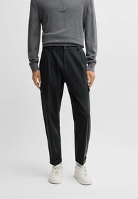 Szara bluzka z długim rękawem o teksturowanym wykończeniu i półguzikowym kołnierzyku, w połączeniu z ciemnymi spodniami w paski i białymi sneakersami.