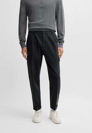 Grå långärmad topp med texturerad yta och halvknapstigning, kombinerad med mörka randiga byxor och vita sneakers.