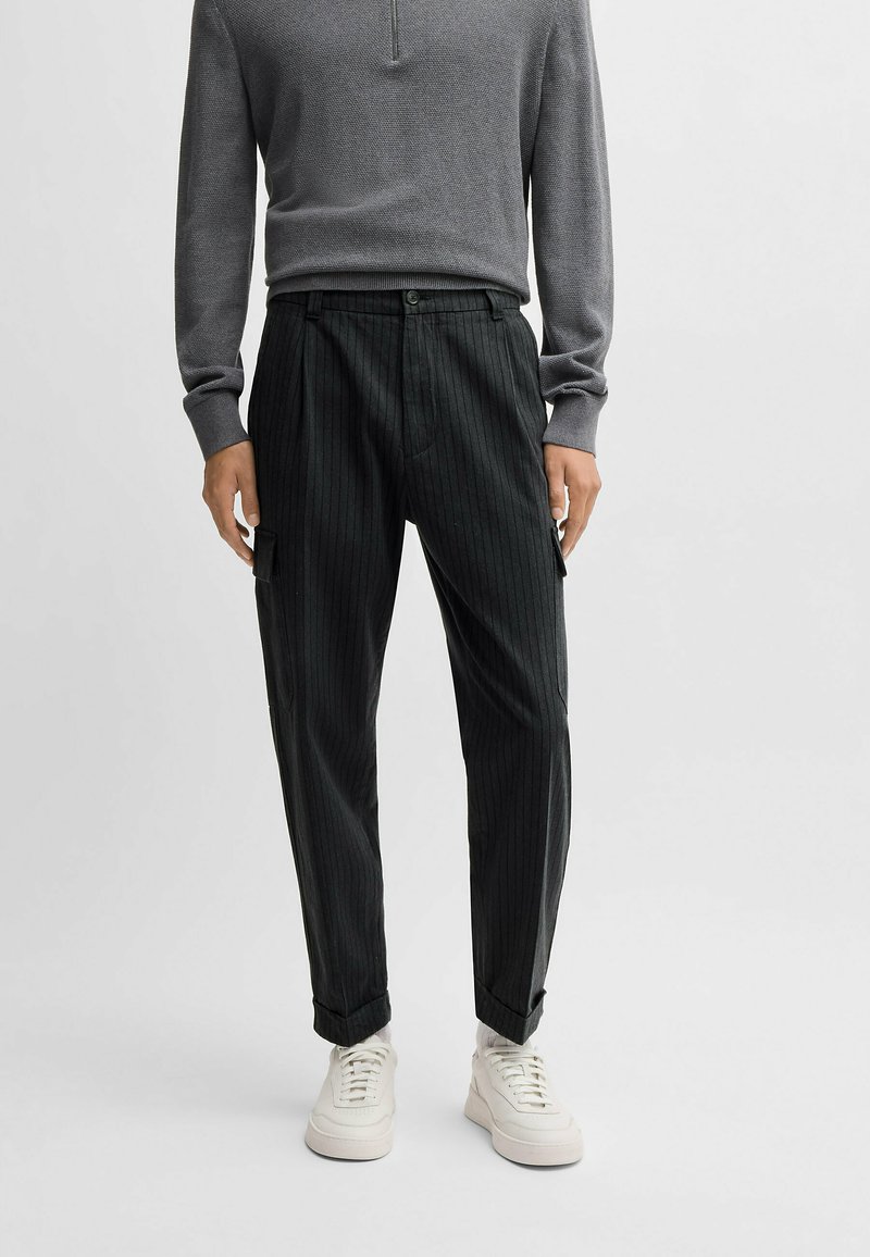 Szara bluzka z długim rękawem o teksturowanym wykończeniu i półguzikowym kołnierzyku, w połączeniu z ciemnymi spodniami w paski i białymi sneakersami.