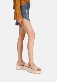 Sandali platform beige con cinturini intrecciati, fibbia alla caviglia color tan e suola bianca texturizzata a motivo, abbinati a una gonna di jeans e a un top in maglia.