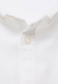 Chemise blanche à boutons avec un col classique, texture douce, et un seul bouton visible avec une finition lisse. Design simple et épuré.