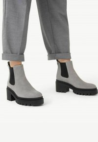 Botas de tobillo de ante gris con paneles laterales elásticos negros y suelas de goma negra gruesas. Presenta una punta redonda y un tacón apilado para mayor estabilidad.