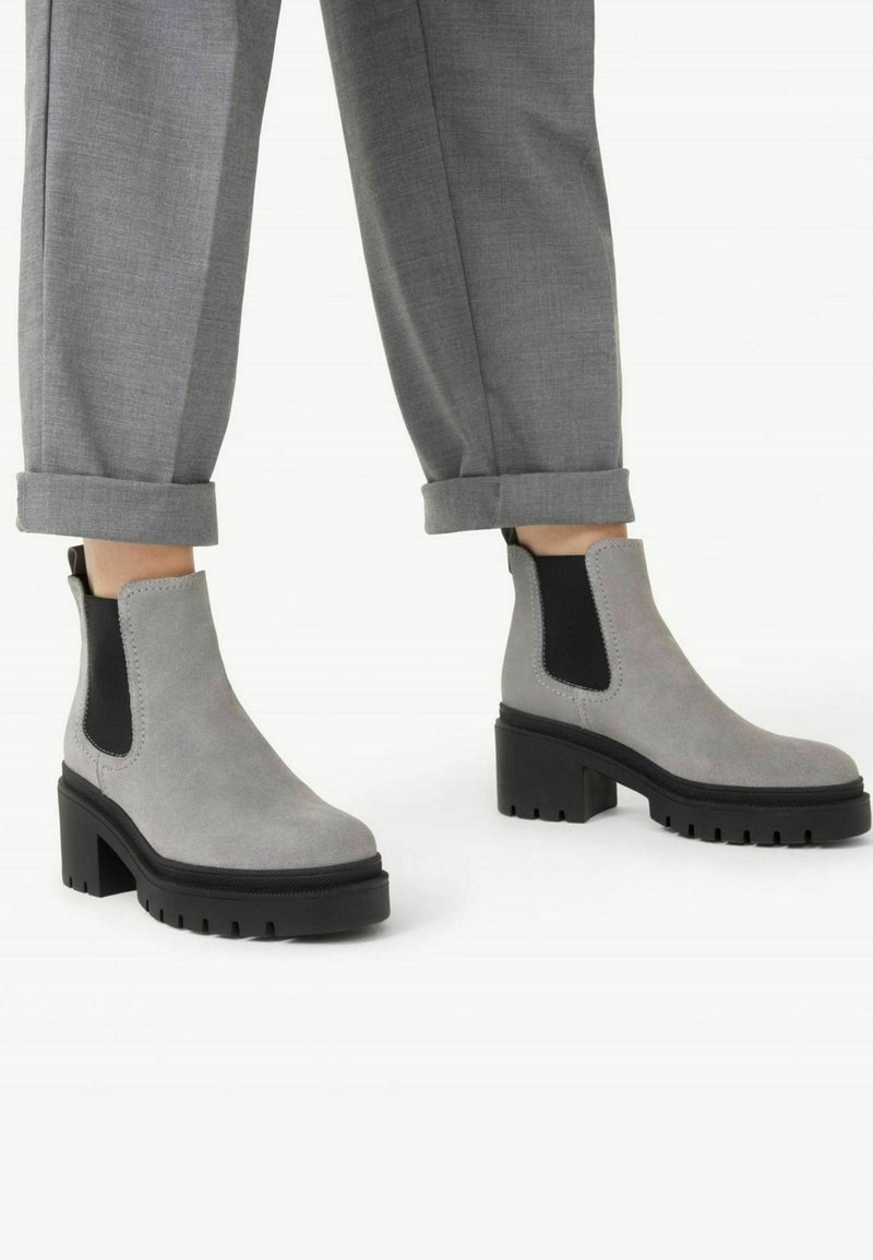 Botas de tobillo de ante gris con paneles laterales elásticos negros y suelas de goma negra gruesas. Presenta una punta redonda y un tacón apilado para mayor estabilidad.