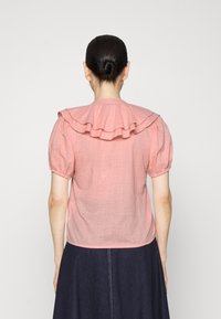 Blusa de linho rosa com detalhes de renda na gola, mangas curtas bufantes e um tecido leve e texturizado, combinada com uma saia de ganga escura.