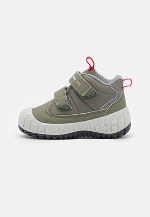 Zielone buty z tkaniny z szarymi akcentami, dwiema regulowanymi zapięciami na rzepy, teksturowanym białym czubkiem z gumy oraz czerwonym uchwytem na pięcie.