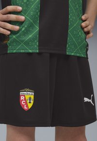 Musta spordivorm, millel on pealmisel osal tekstureeritud roheline muster ja Racing Club de Lens'i logo. Sisaldab valget Puma brändingut.