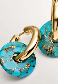 Los pendientes circulares turquesa presentan acentos de metal de color dorado con destellos dorados visibles incrustados en la piedra, realzando la superficie texturizada.