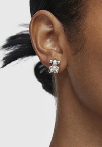 Orecchini in argento a forma di orso presentano una perla centrale, con superfici lisce e bordi arrotondati. Imitati su un orecchio di un modello.