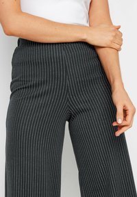 Zwarte wijde broek met witte verticale strepen, met een gladde textuur en een hoge taille. Minimalistische en gestructureerde uitstraling.