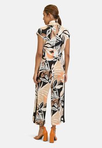 Tuta floreale con maniche corte, realizzata in tessuto leggero. Presenta un motivo di foglie nere, beige e arancioni. Abbinata a tacchi a blocco arancioni.