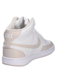 Sneaker alte bianche e beige in pelle e rete con suola in gomma e logo Nike ben visibile sul retro.