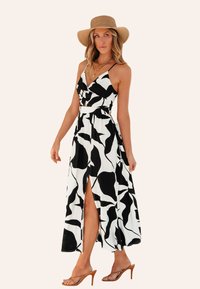 Abito lungo in bianco e nero con motivo astratto, caratterizzato da una profonda scollatura a V, spalline regolabili e uno spacco alto fino alla coscia. Tessuto in satin; sandali eleganti.