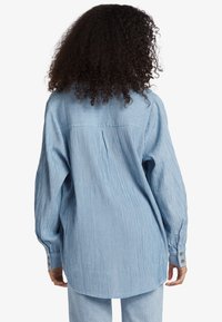 Blue and white striped collared shirt with long sleeves, buttoned cuffs, and back yoke detail. Made of light fabric, featuring a relaxed fit.