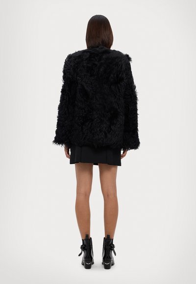 Black faux fur jacket with long sleeves, textured surface, and relaxed fit, worn over a short skirt and heeled ankle boots.