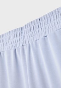 Tissu bleu clair avec une large ceinture élastique présentant plusieurs rangées de coutures, créant une texture froncée et extensible.