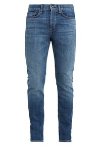 Jeans de mezclilla azul de corte ajustado con un efecto desgastado, diseño de cinco bolsillos y costuras en contraste. Textura suave con un aspecto ligeramente usado.
