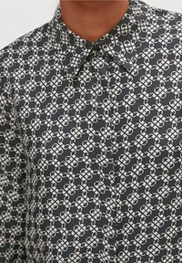 Chemise boutonnée en tissu à motif avec un fond noir et des dessins blancs entrelacés, dotée d'un col classique.