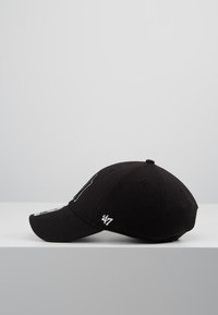 Svart caps med buet skjerm, laget av stoff. Har hvit brodert tekst og logo accenter. Designet er enkelt og sporty.