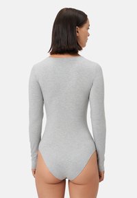 Body z długim rękawem w jasnoszarym kolorze, wykonany z gładkiej, elastycznej tkaniny. Posiada wycięcie na plecach w kształcie litery U oraz dopasowany krój.