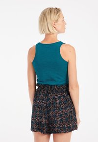 Teal tanktop met een ronde hals, gecombineerd met zwarte shorts met een kleurrijk bloemenpatroon en een elastische tailleband.