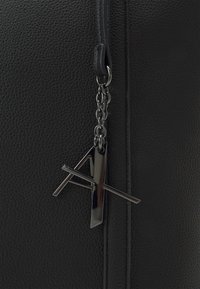 Black leather bag with a textured finish. Features a metal zipper and a silver logo keychain attached by a chain.