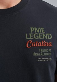 Námořnické bavlněné tričko se zeleným a oranžovým vyšitým textem: "PME LEGEND," "Catalina," a "Tested at High Altitude," s vlnkovými vzory.