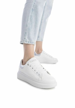 Zapatillas blancas hechas de material sintético, con una textura suave, punta redondeada y una suela gruesa. Diseño con cordones y acentos mínimos.