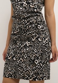 Robe imprimée léopard noire avec un design ajusté, une texture froncée et une coupe mi-genou, agrémentée d'accents marron et blanc.