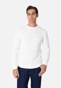 Maglione lavorato a maglia di colore crema con un motivo a nido d'ape, scollatura rotonda e polsini a costine, abbinato a jeans di jeans blu.