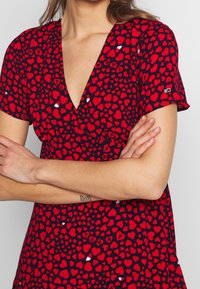 Vestido rojo y negro con un patrón de corazones, escote en V profundo, mangas cortas y un diseño ajustado.