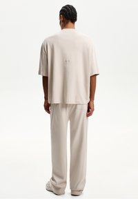 Beige oversized t-shirt with a round neckline and short sleeves, paired with matching loose-fitting trousers. Material appears soft and smooth.