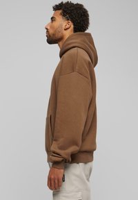 Sweat-shirt à capuche marron avec une coupe décontractée, poches latérales et poignets côtelés. Tissu doux avec une finition mate. Design uni, sans motifs.