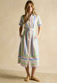 Gestreiftes Hemdblusenkleid mit kurzen Ärmeln, in sanften Farben, mit einem Taillengürtel und seitlichen Taschen. Der Stoff wirkt leicht und strukturiert.